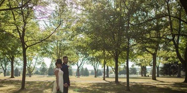 A couple standing together in the open grove on the grounds, late afternoon light through the trees
