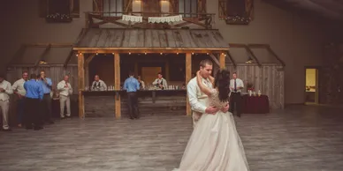 A couple sharing their first dance on the Stone Hall floor, guests and the bar behind them