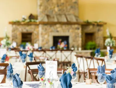 Round tables in white linen with slate-blue napkins set in front of the Stone Hall's stone fireplace